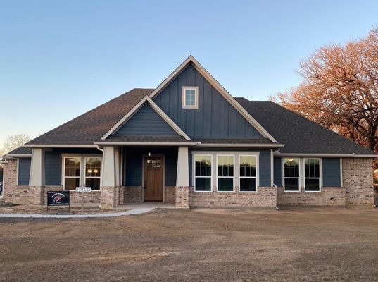 A newly constructed single-story home with blue vertical siding, brick accents, a brown roof, and a covered entryway.
