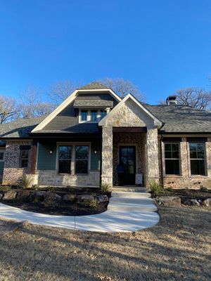 A single-story home with tan stone and teal siding, a shingled roof, a stone-accented entrance, and a concrete walkway.