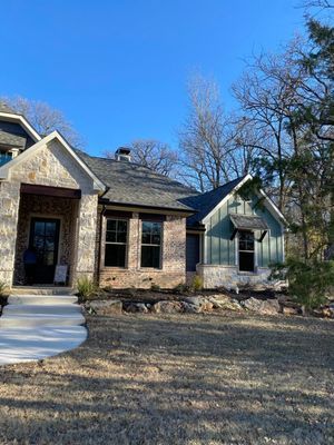 A single-story home exterior featuring light-colored stone, green board-and-batten siding, and a gabled roof under a blue sky.