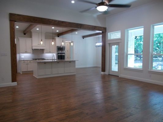 A spacious open-concept kitchen and living area with white cabinets, a large island, wooden beams, and hardwood floors.