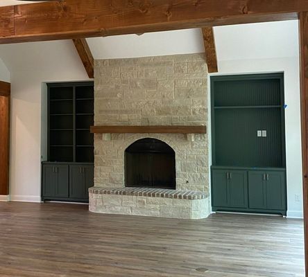 A stone fireplace with a wooden mantel sits between two dark green built-in cabinets in a room with wood-look flooring.