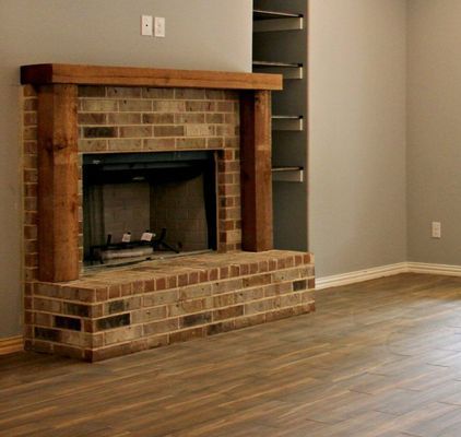 A brick fireplace with a thick wooden mantle and two wooden pillars, set against a grey wall with nearby built-in shelves.