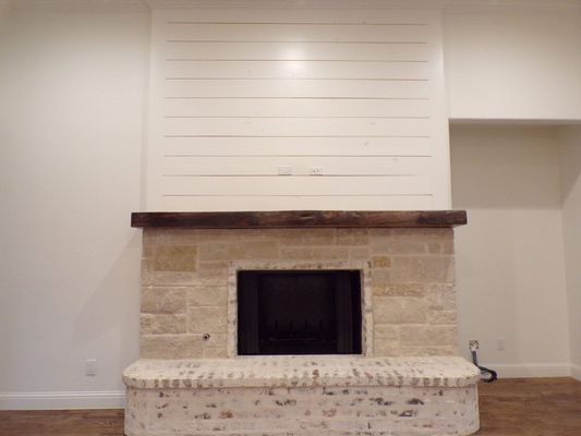 A fireplace with a white shiplap top section, a dark wood mantel, a stone middle, and a white brick hearth base.