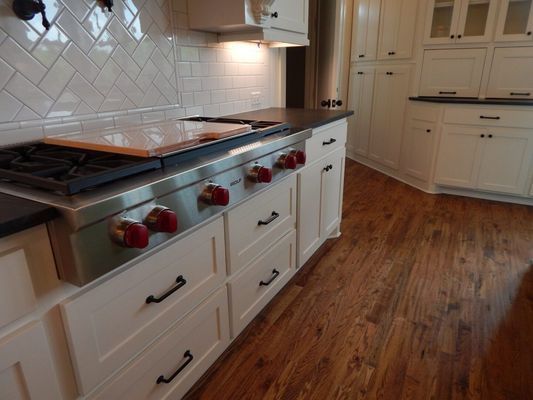 A high-end kitchen with white cabinets, a professional-style stainless steel gas range, and dark wood flooring.