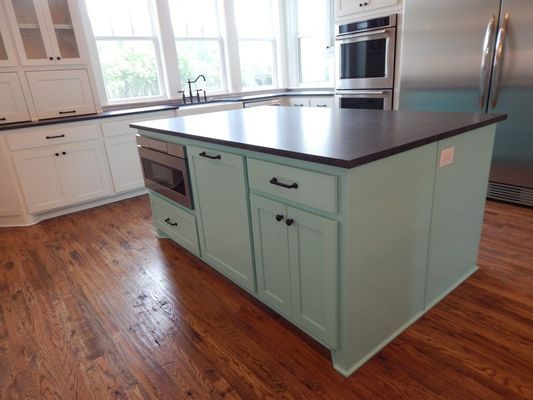 A kitchen island with a dark countertop and mint green cabinets, set on wood floors in a bright, modern kitchen.