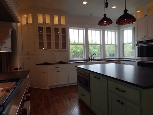 A kitchen with white cabinets, dark countertops, a mint-green island, and pendant lighting over a window-filled wall.