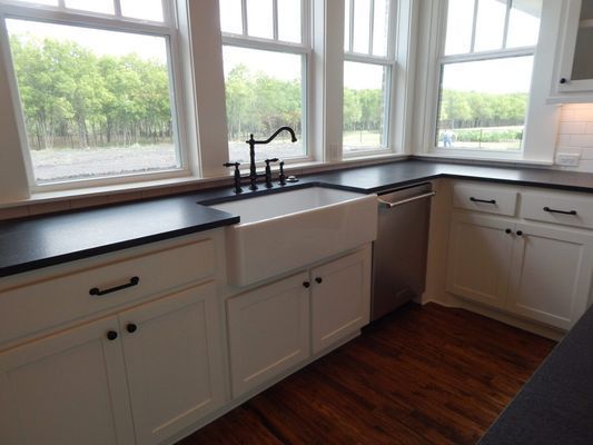 A white farmhouse sink with a black faucet set into black countertops above white cabinets in a bright kitchen.