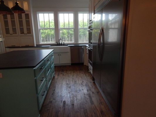 A kitchen with a teal island, dark countertops, wood floors, white cabinets, and a stainless steel refrigerator.