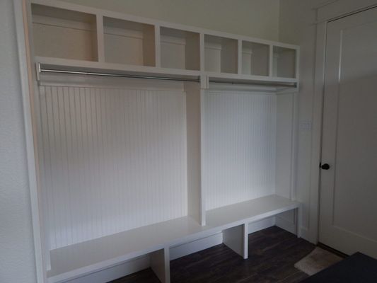 White custom mudroom built-in unit with bench seating, coat racks, and upper cubbies, positioned near a doorway.