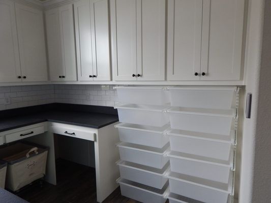White storage cabinets and a dark countertop workspace with white plastic bins stacked against the side wall.