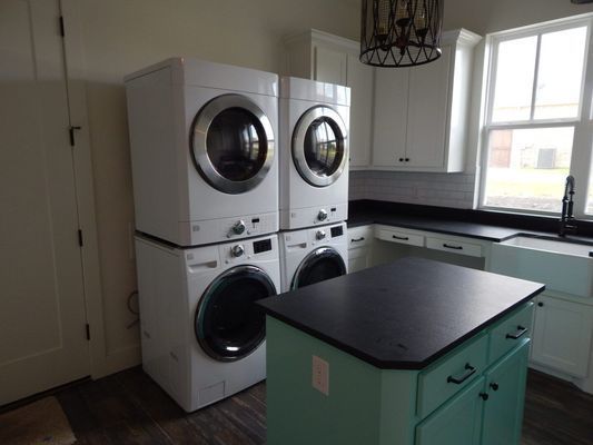 A laundry room featuring two white stacked washer-dryer units next to a light blue island with a dark countertop.