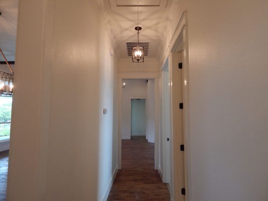 A hallway with light walls, wood-look flooring, and a decorative pendant light fixture, looking into another room.