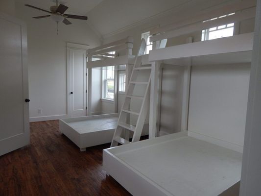 A room with white wood floors features two sets of white bunk beds separated by a central wooden ladder.