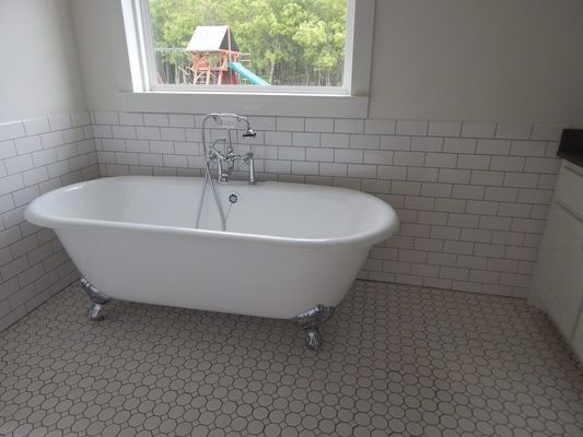 A white clawfoot bathtub with a chrome faucet in a bathroom with white subway tile walls and small hexagonal floor tiles.