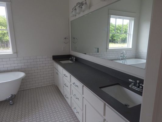A modern bathroom featuring a white clawfoot tub, double vanity with dark countertops, white cabinetry, and subway tile.