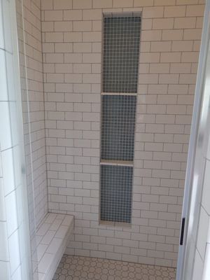 A shower stall with white subway tile walls, a built-in bench, and a vertical recessed niche with mosaic tile shelving.