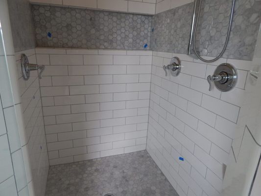 A shower stall with white subway tile walls, a grey pebble-tile floor and accent strip, and chrome shower fixtures.