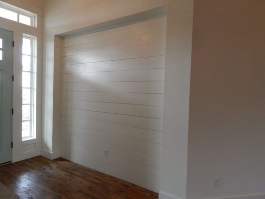 An interior entryway featuring a recessed wall with white horizontal shiplap paneling and dark hardwood flooring.