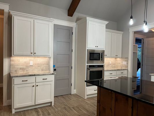 A kitchen with white cabinets, light wood floors, a grey door, and a built-in oven and microwave unit.