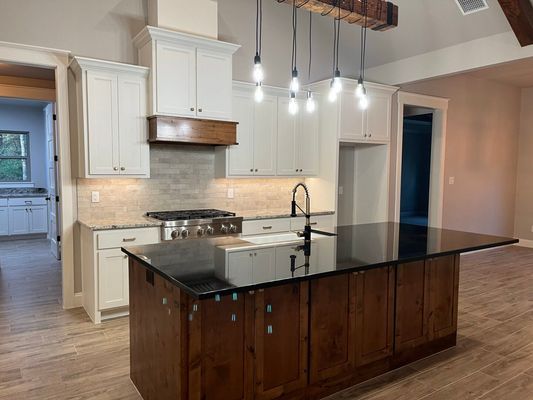 Modern kitchen with white upper cabinets, dark wood kitchen island, black countertops, and a wooden pendant light fixture.