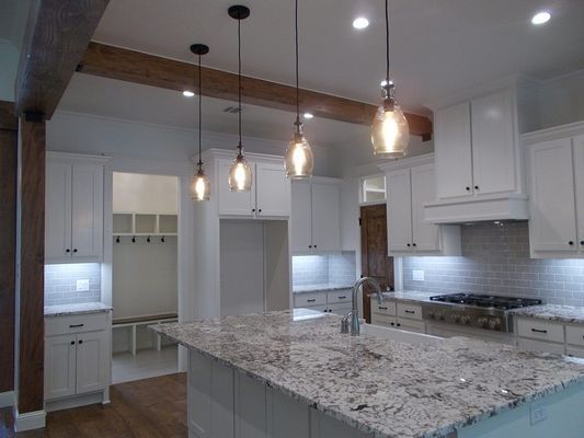 A bright, modern kitchen featuring white cabinets, granite countertops, a large island, and four hanging pendant lights.