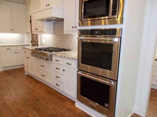 A bright kitchen featuring white cabinets, stainless steel double wall ovens, a microwave, and a gas stove on granite.