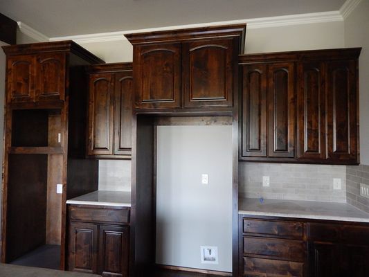 Dark wood kitchen cabinets with crown molding, featuring a built-in refrigerator space and counter space on either side.