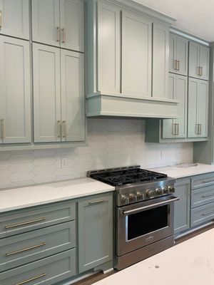 A kitchen with light green cabinetry, white countertops, a professional-style stainless steel oven, and a tiled backsplash.