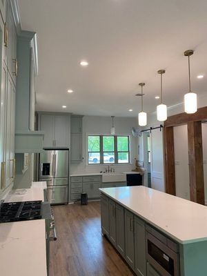 A modern kitchen with light blue-grey cabinets, a central island, stainless steel appliances, and three pendant lights.