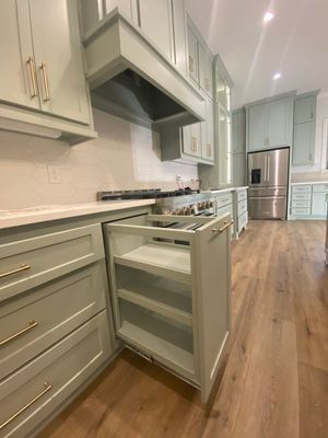 A modern kitchen features light green cabinetry with gold hardware, including a pull-out spice rack near a gas stove.