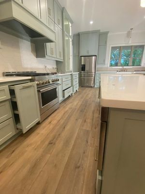 A modern kitchen with sage green cabinets, light wood floors, a stainless steel stove, and a large white-topped island.