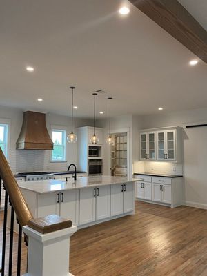 A bright, modern kitchen featuring a large white island with pendant lights, a copper range hood, and hardwood floors.