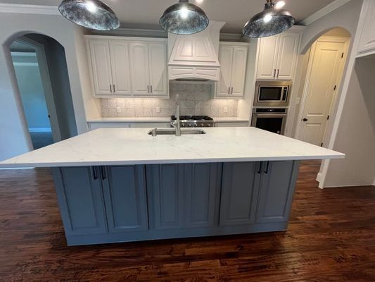 A modern kitchen featuring a large central island with grey cabinets and a white countertop, under three pendant lights.