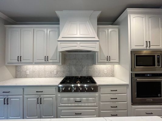 A white kitchen with shaker cabinets, a stainless steel gas range, a custom range hood, and a built-in oven and microwave.