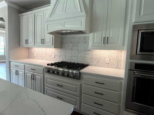 Modern kitchen featuring white cabinets, a gas range with a decorative hood, marble-patterned countertops, and a wall oven.