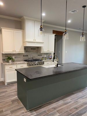 Modern kitchen featuring a large dark gray island, white cabinetry, stainless steel appliances, and wood-look flooring.