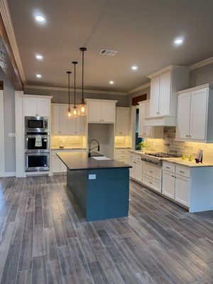 Modern kitchen featuring white cabinets, a dark blue island, stainless steel appliances, and wood-look tile flooring.