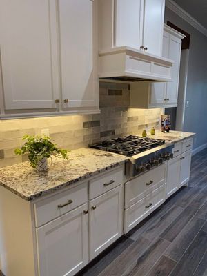 A modern kitchen with white cabinets, speckled granite countertops, a gas stove, and a tiled backsplash.