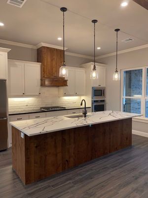 Modern kitchen with a dark wood island, white cabinets, marble-patterned countertops, and three hanging pendant lights.