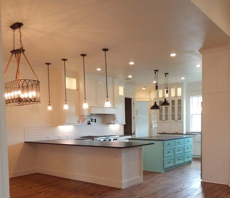 A kitchen with white cabinets, dark countertops, a teal island, pendant lights, and a hanging metal lantern chandelier.