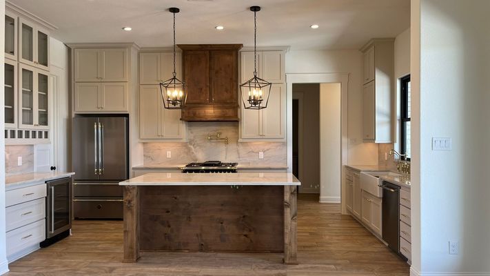 Modern kitchen featuring a large wooden island, light-colored cabinetry, stainless steel appliances, and pendant lighting.