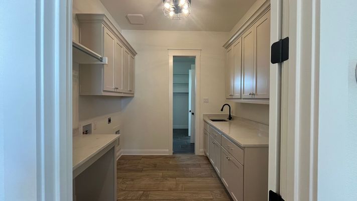 A laundry room with light-colored cabinets, quartz countertops, a small sink, and wood-look tile flooring.