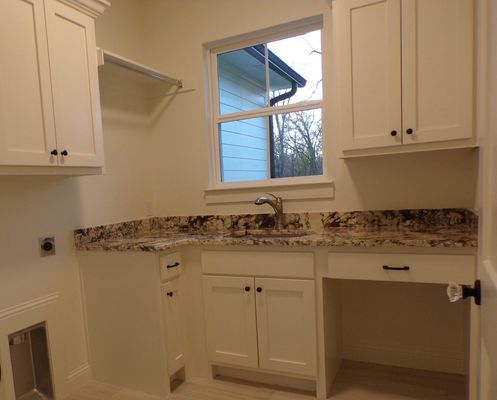 Laundry room with white cabinets, speckled granite countertops, a stainless steel sink, and a window above the sink.