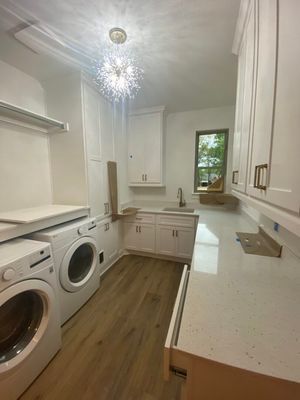 A bright, modern laundry room with white cabinets, light quartz countertops, front-load washers, and wood-look flooring.
