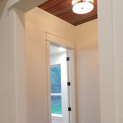 A hallway with white walls and a wood-slat ceiling, leading to a door showing a window with an outdoor view.