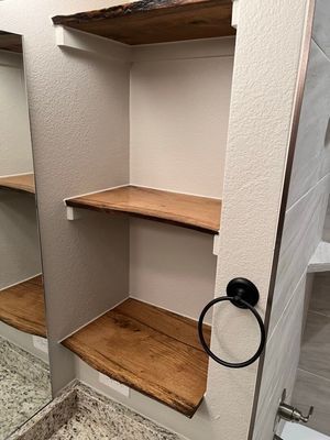 A bathroom wall niche with three rustic, live-edge wood shelves, featuring a black circular towel ring mounted on the side.