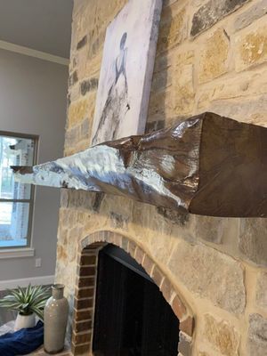 A heavy, textured wooden fireplace mantel mounted on a light stone chimney breast below a framed artwork.