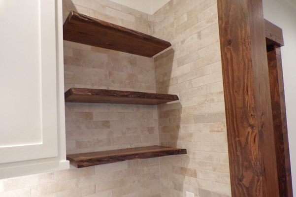 Three wooden shelves with natural live edges mounted on a light-colored, textured stone wall next to a white cabinet.