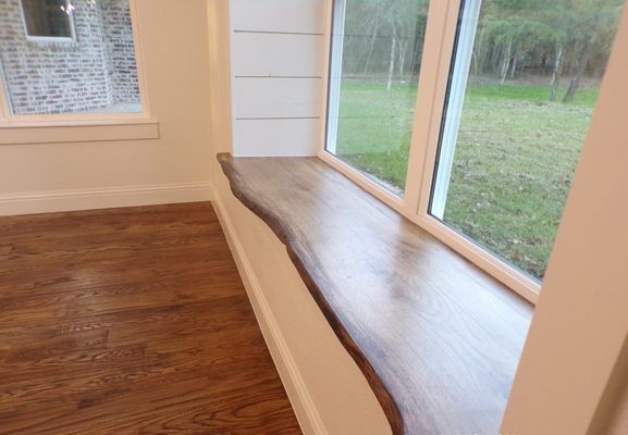 A live-edge wood window sill with a natural finish installed in a room with white shiplap walls and hardwood flooring.