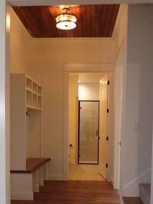 A hallway with a built-in white mudroom bench, a wood-paneled ceiling, a light fixture, and an open door to a bathroom.